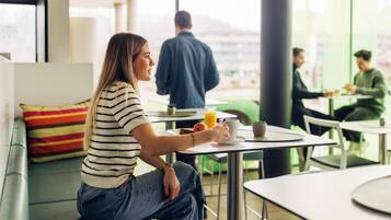 Une personne assise sur un canapé vert, avec un coussin à rayures, tenant une tasse et une soucoupe.