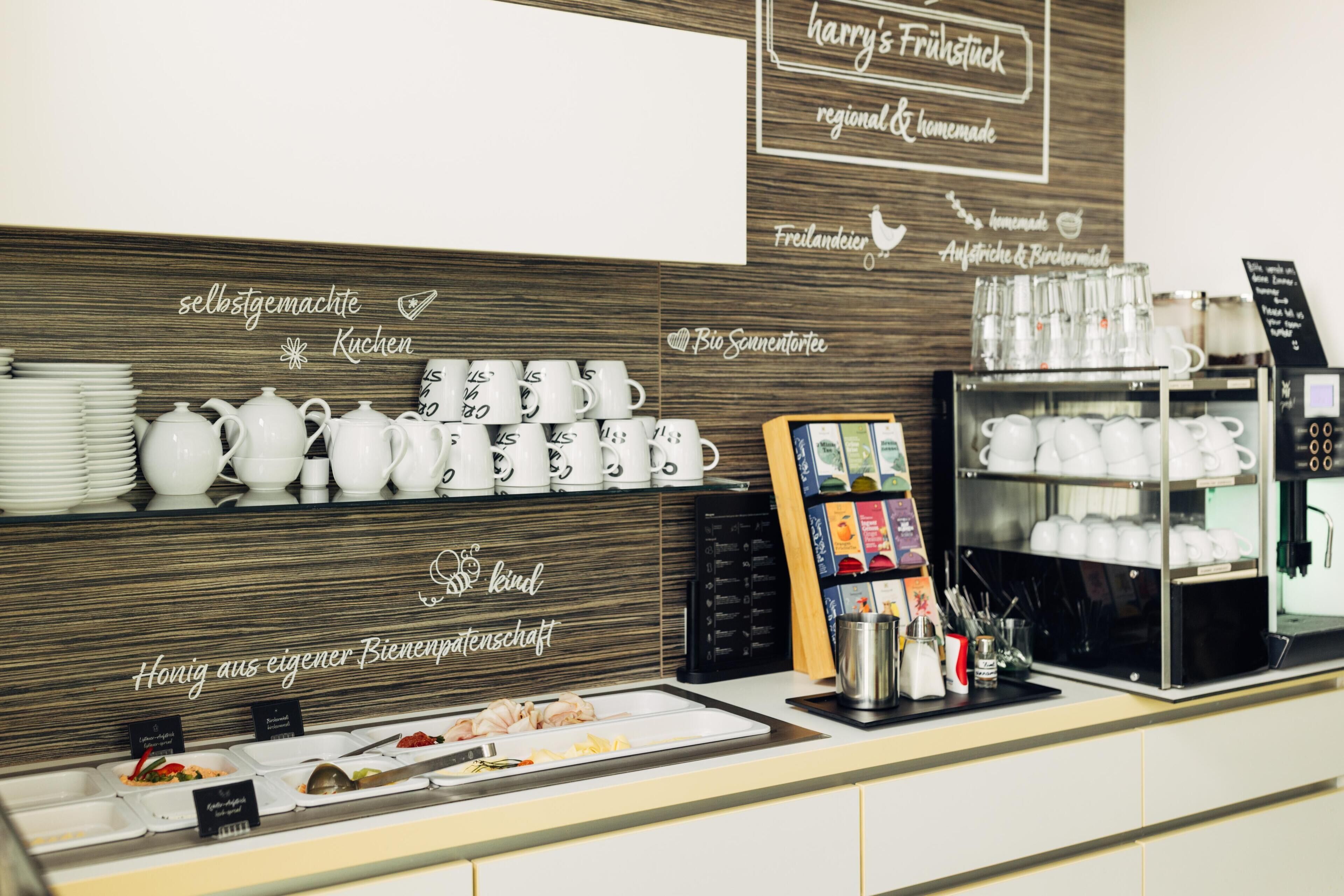 A breakfast buffet area with white ceramic dishes, a coffee machine, and a sign indicating homemade regional products.