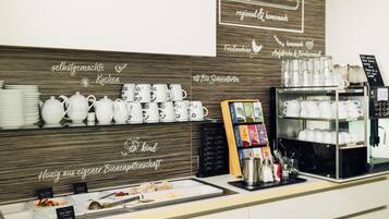 A breakfast buffet area with white ceramic dishes, a coffee machine, and a sign indicating homemade regional products.