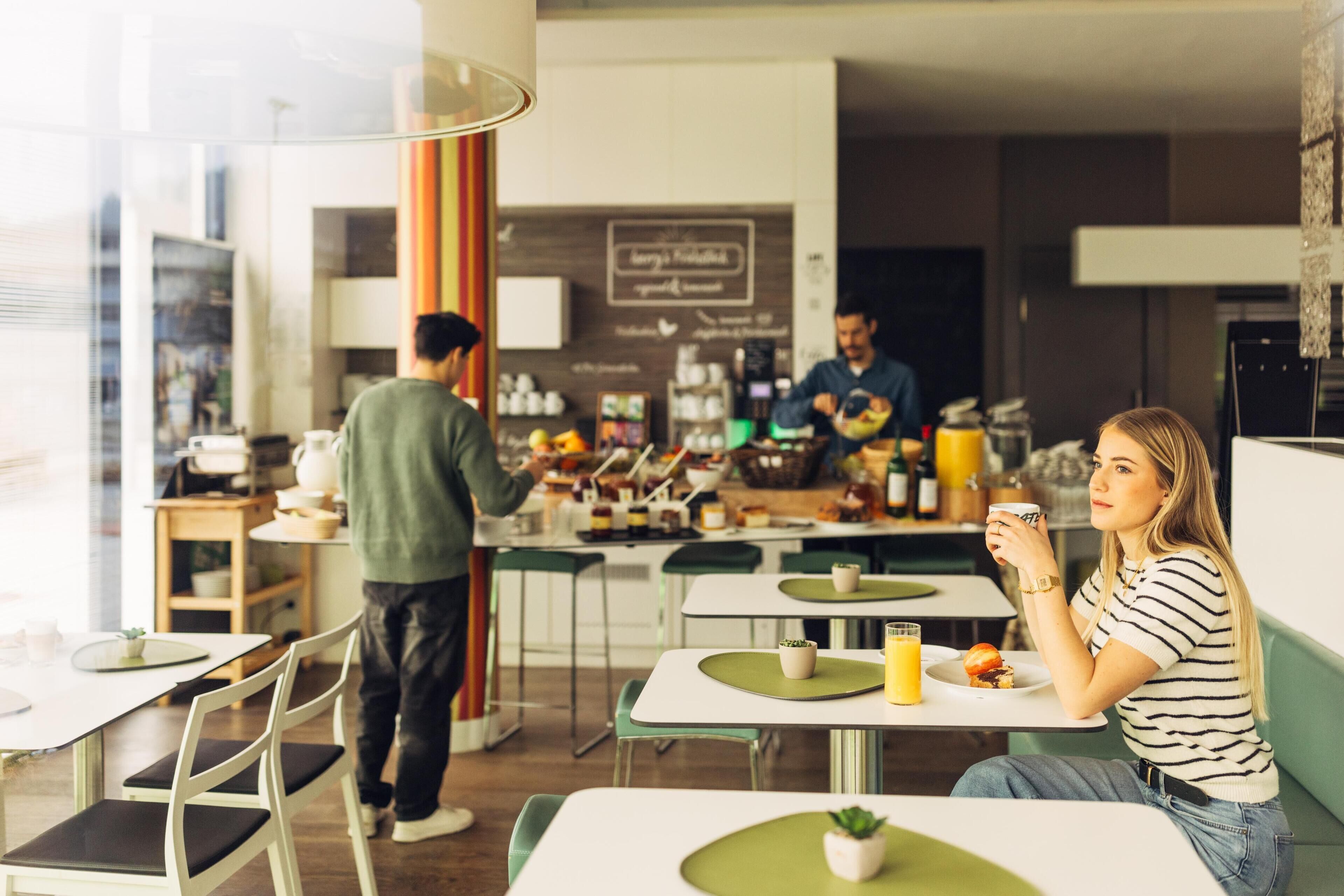 A modern cafe with tables and chairs, a counter with a menu, and a person serving food.