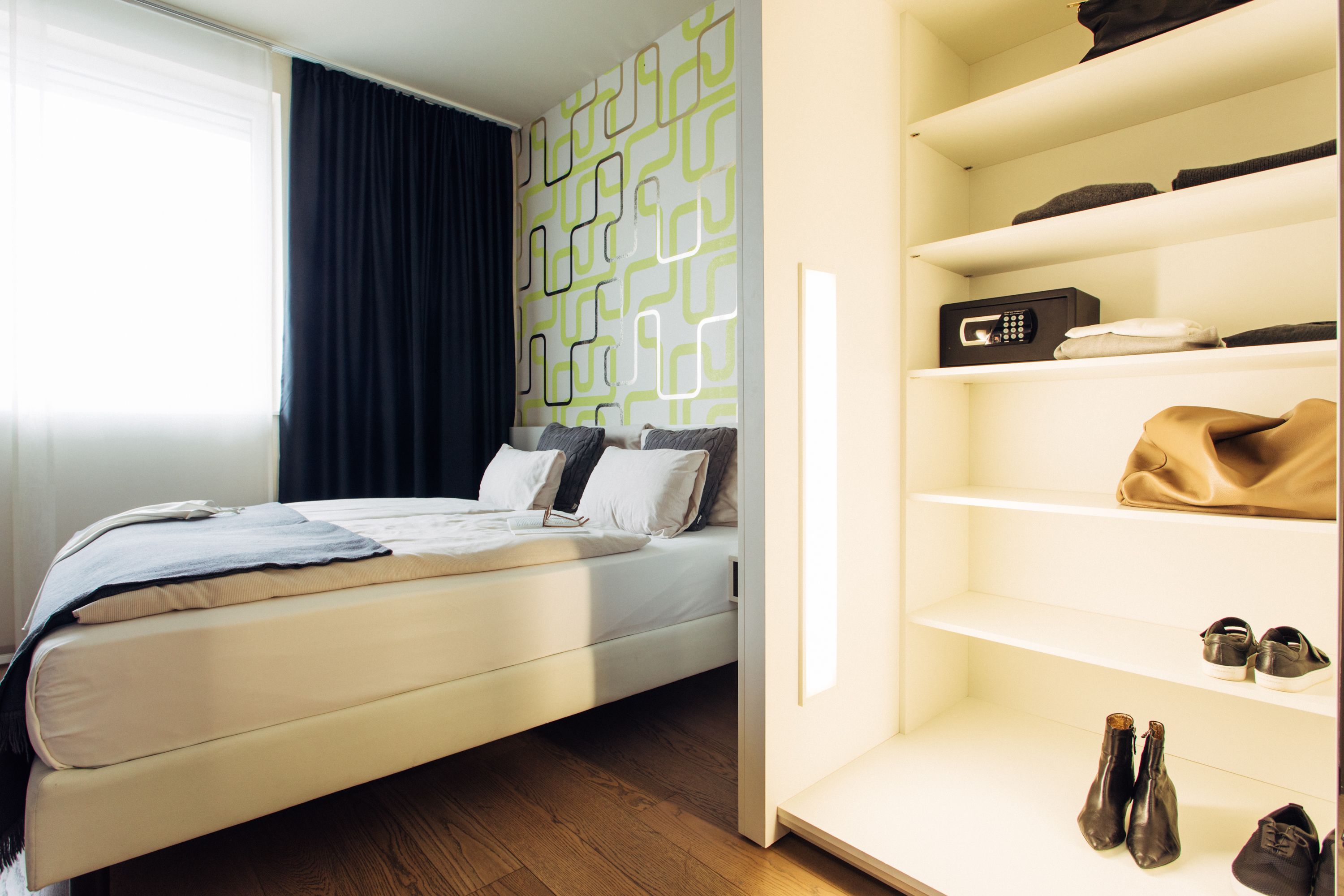 A modern bedroom with a bed, a wardrobe with shelves, and a window with curtains.