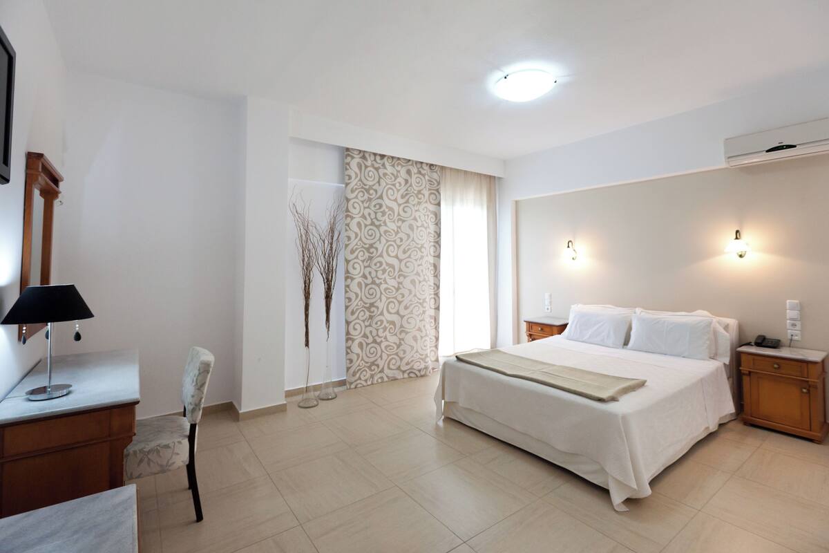 Een hotelkamer met een bed, nachtkastje, lamp, stoel en decoratief wandpaneel.