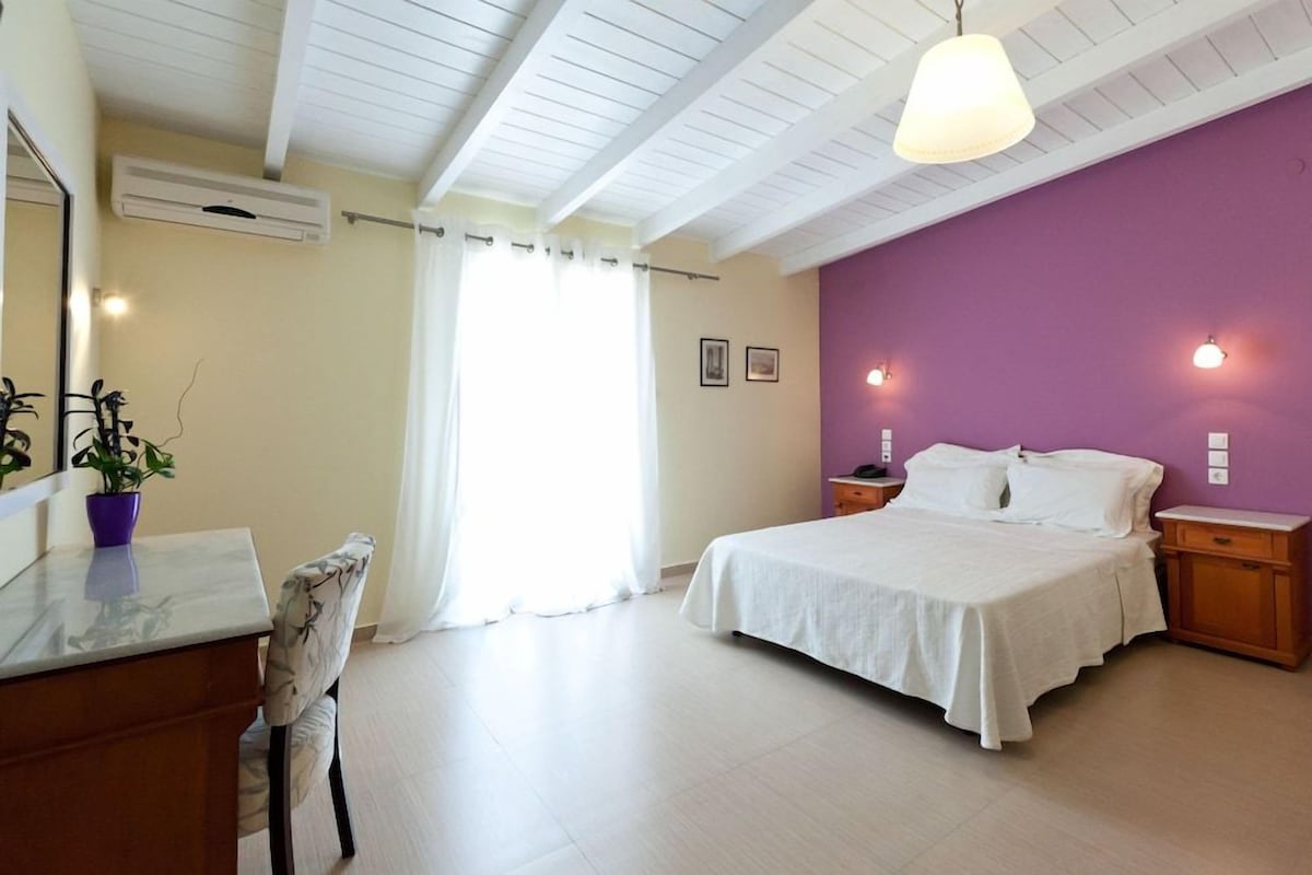 Une chambre à coucher comprenant un lit, des tables de chevet, un bureau avec une chaise, un climatiseur et une fenêtre avec des rideaux.