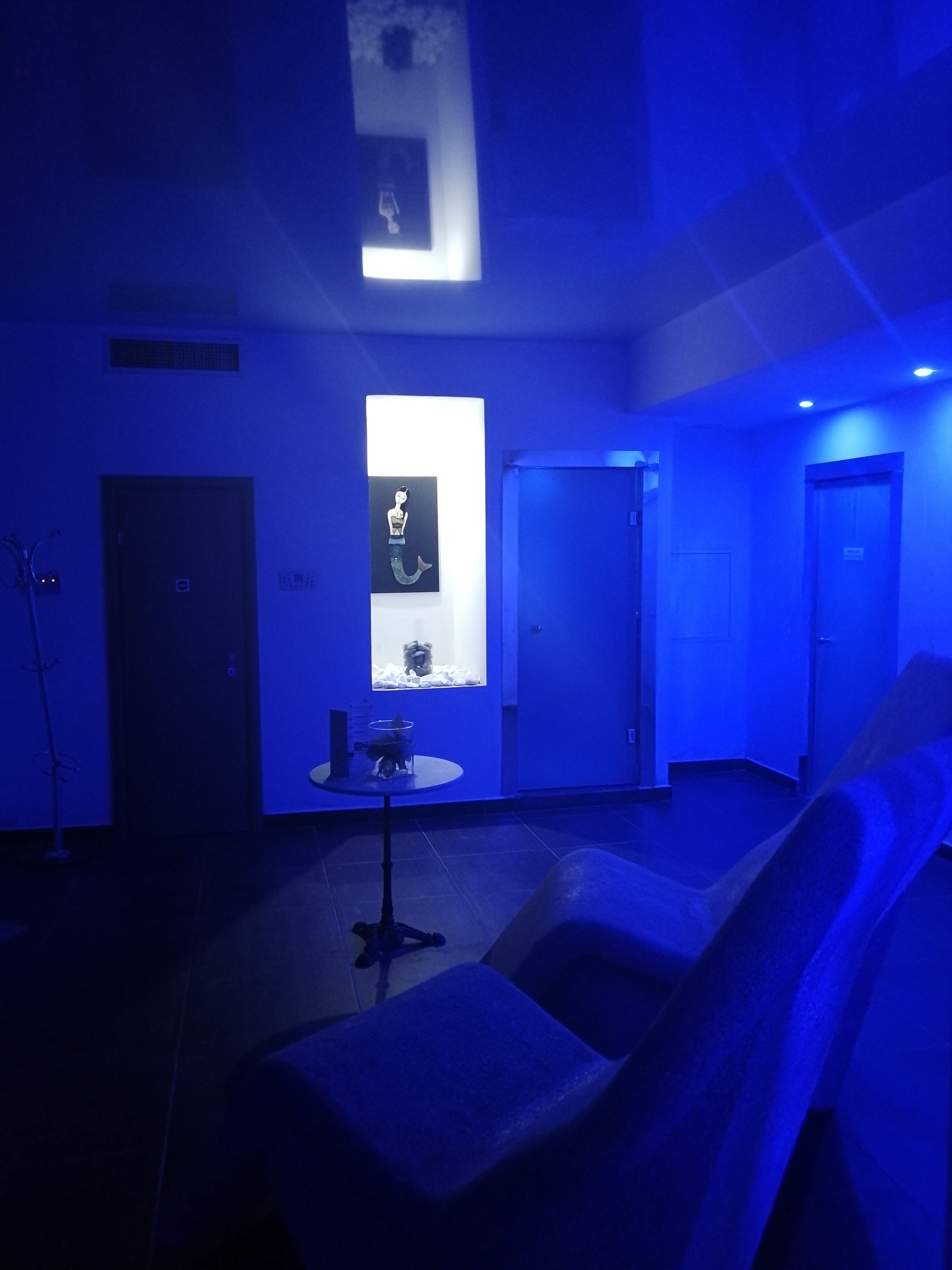 A room with a blue hue, featuring a sofa, a table with a small sculpture, and a framed picture on the wall.