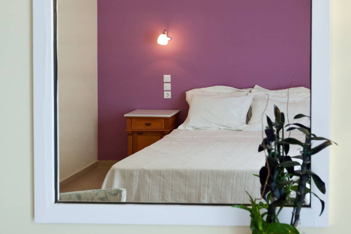 Een slaapkamer met een bed, nachtkastje, lamp en een potplant.