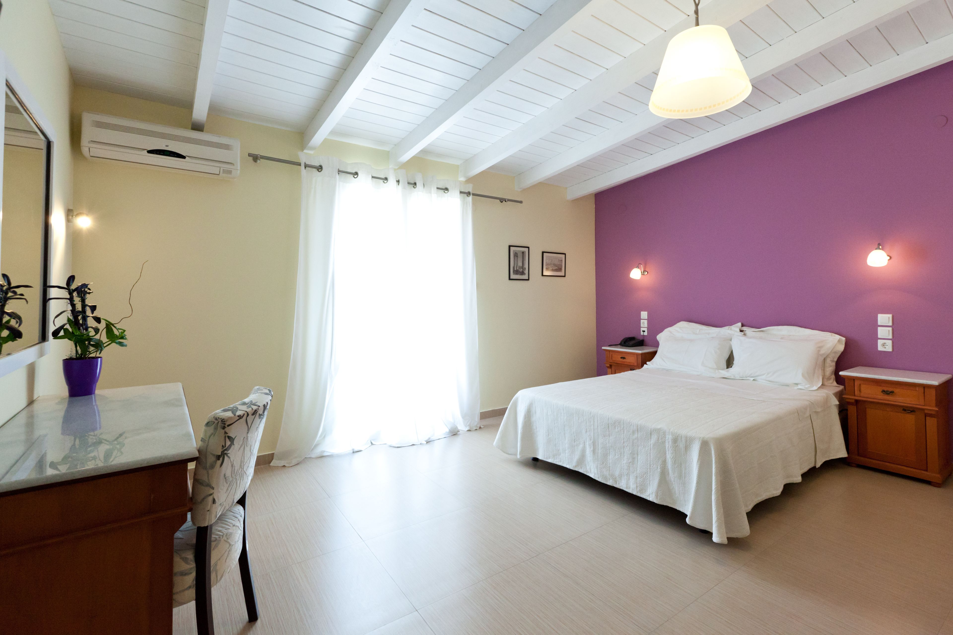 A bedroom with a bed, bedside tables, a desk, a chair, and an air conditioning unit.