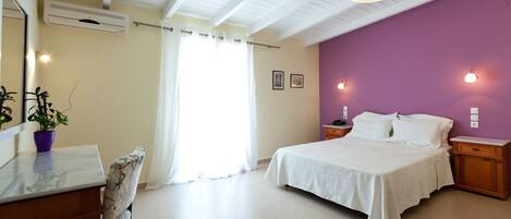 A bedroom with a bed, bedside tables, a desk, a chair, and an air conditioning unit.