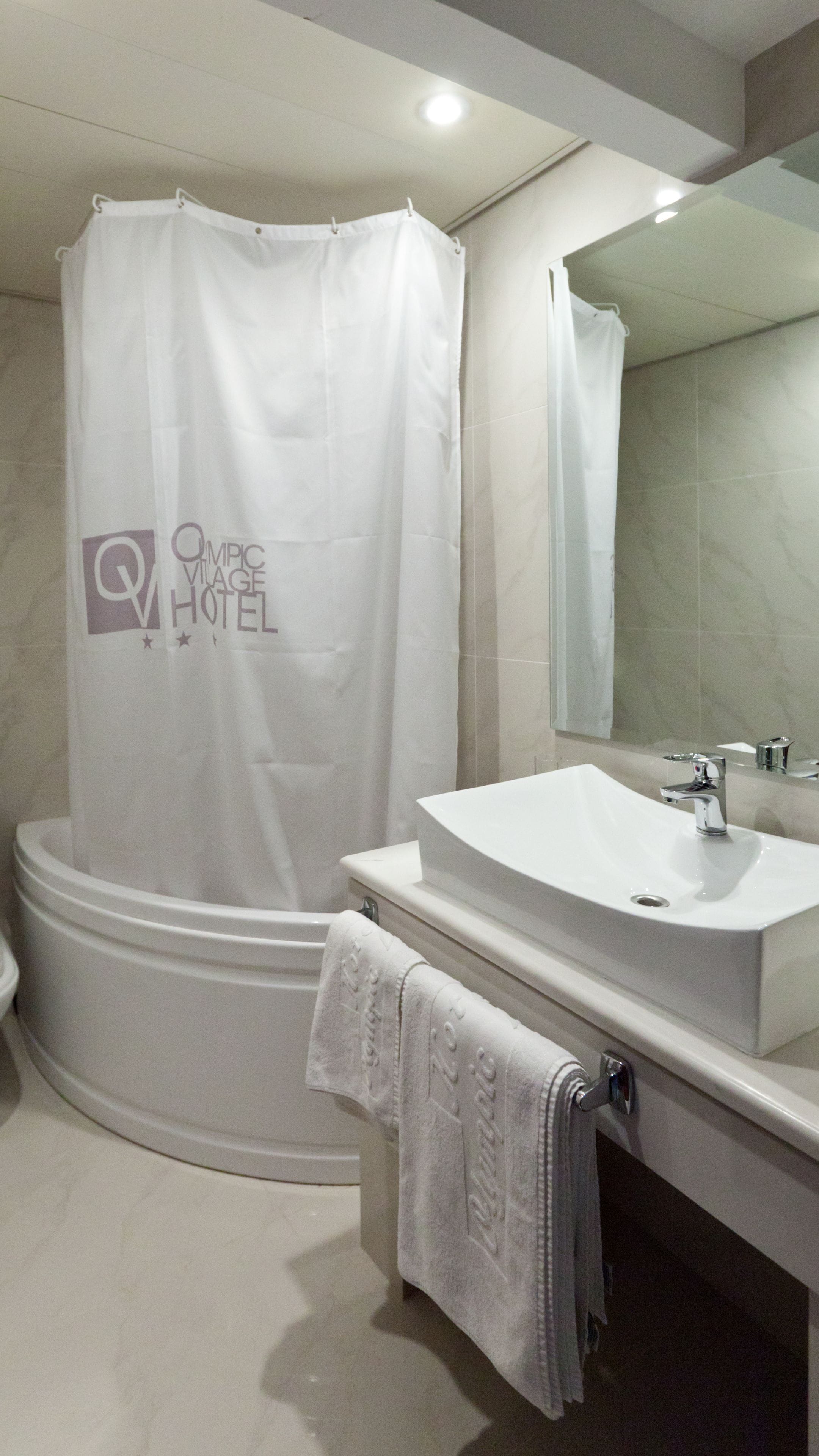 A modern bathroom with a bathtub, a sink, and a shower curtain with a hotel logo.