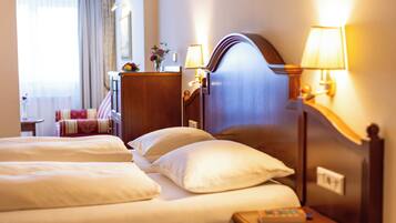 A hotel room with two beds, a wooden headboard, bedside lamps, a nightstand, and a desk with a lamp.