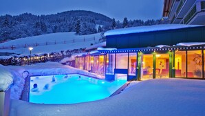 Ein mit Schnee bedeckter Außenpoolbereich mit einer Glaskuppel, umgeben von Schnee und einem Gebäude mit gemütlicher Innenausstattung.