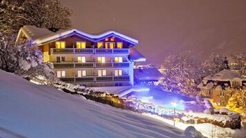 A multi-story hotel with balconies, snow-covered surroundings, and illuminated windows.