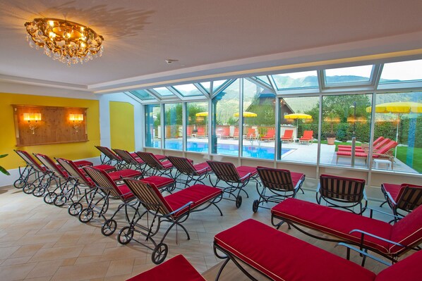 Une pièce baignée de lumière, avec plusieurs rangées de chaises longues et une grande fenêtre donnant sur un espace piscine.