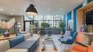 A modern lounge area with seating, a table with a board game, and a TV on the wall. - Appart'City Confort Toulouse Diagora Labège (Labege)