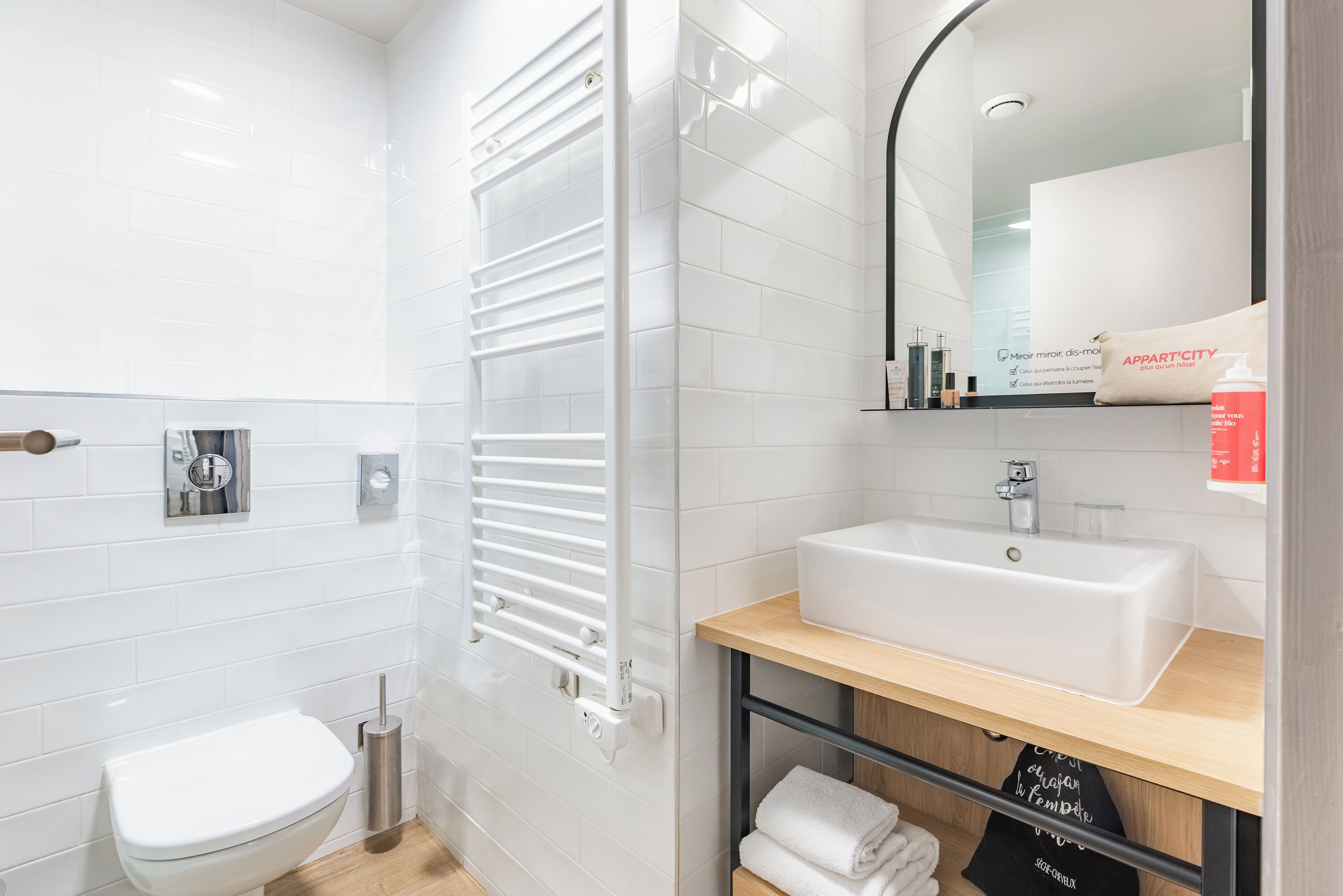 A modern bathroom with a white toilet, a white sink, a towel rack, and a mirror.