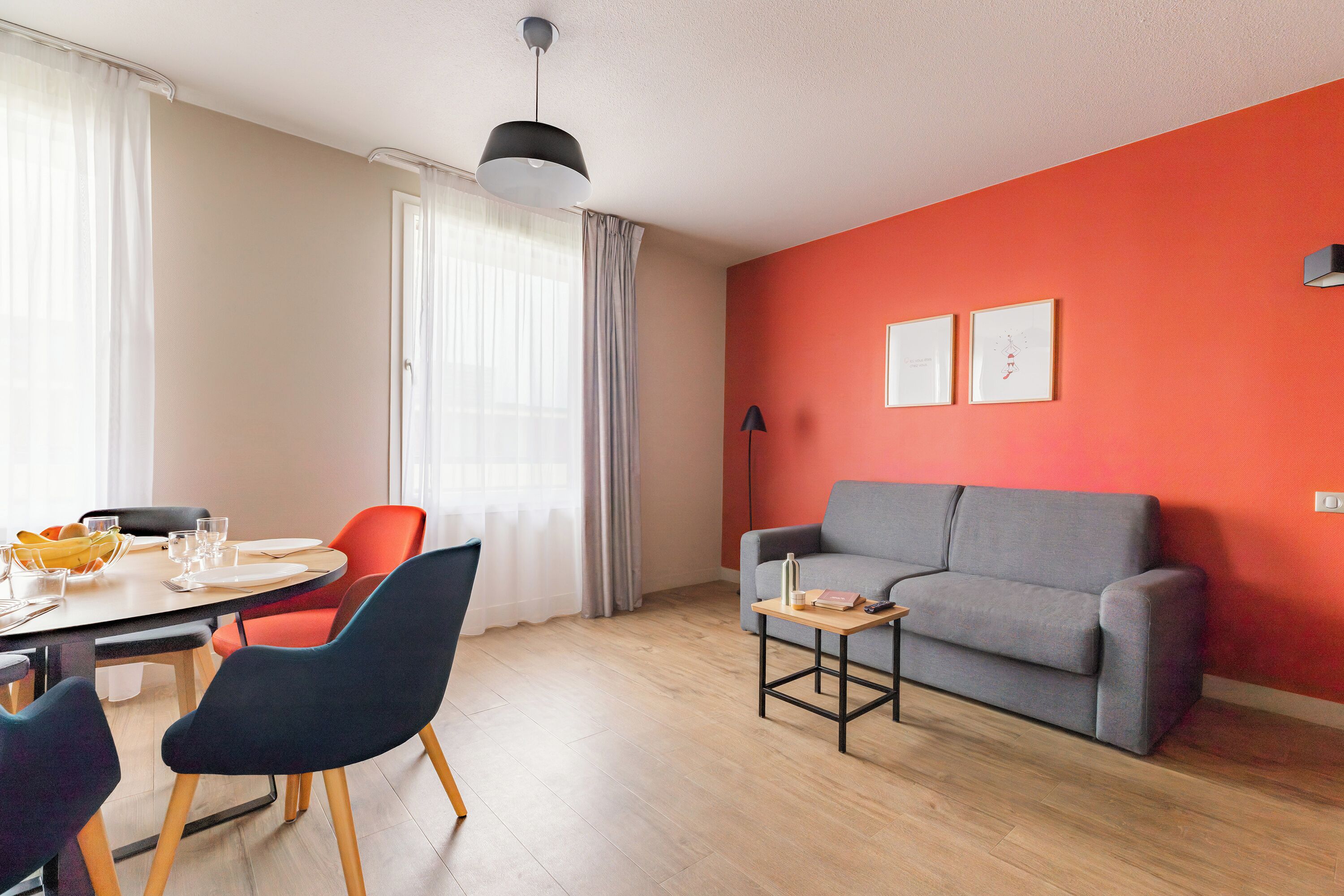 Un salon moderne comprenant un coin repas, un canapé gris et une petite table avec une lampe.