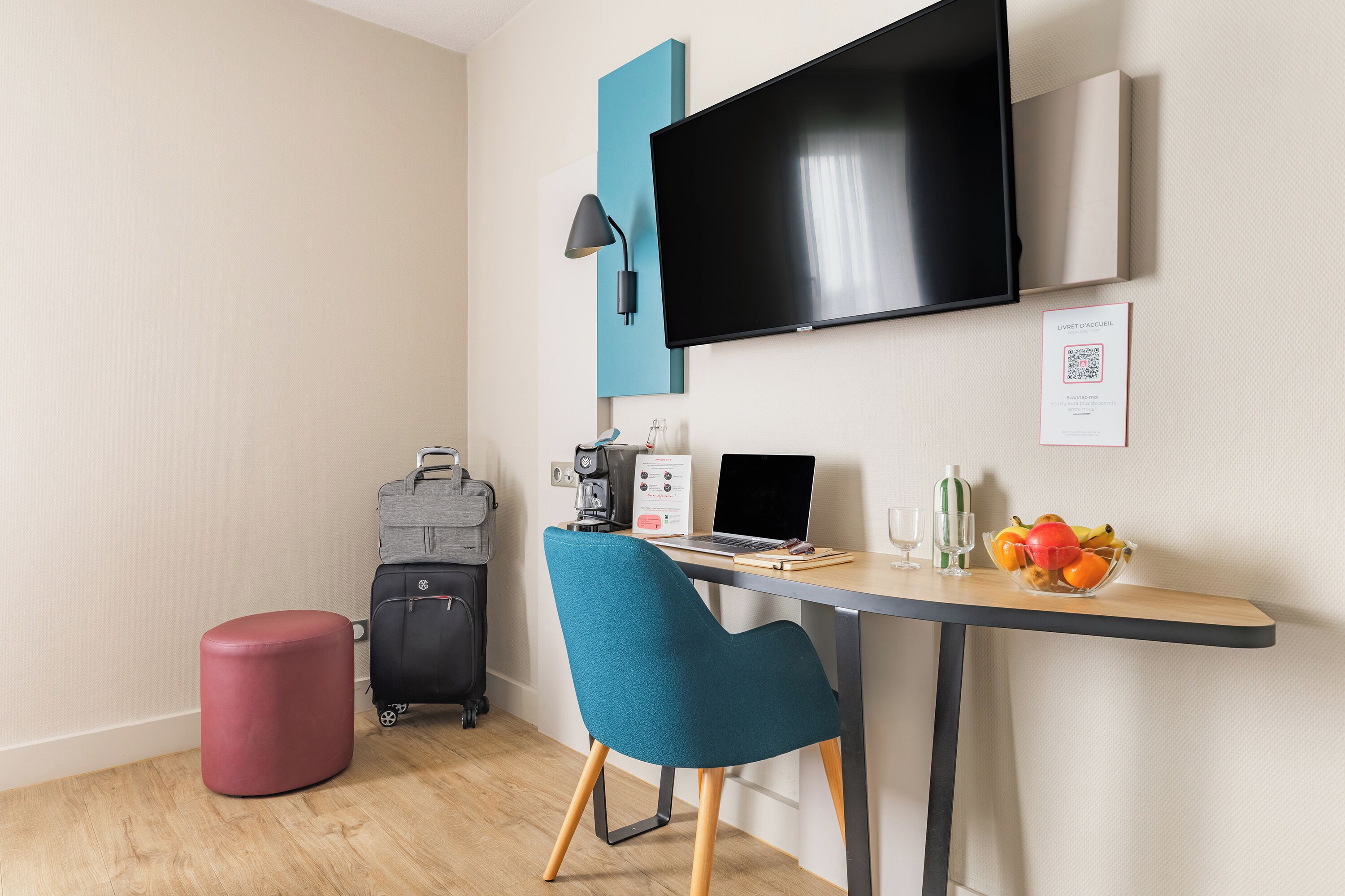 A modern hotel room with a desk, chair, television, and a small table with a fruit bowl.