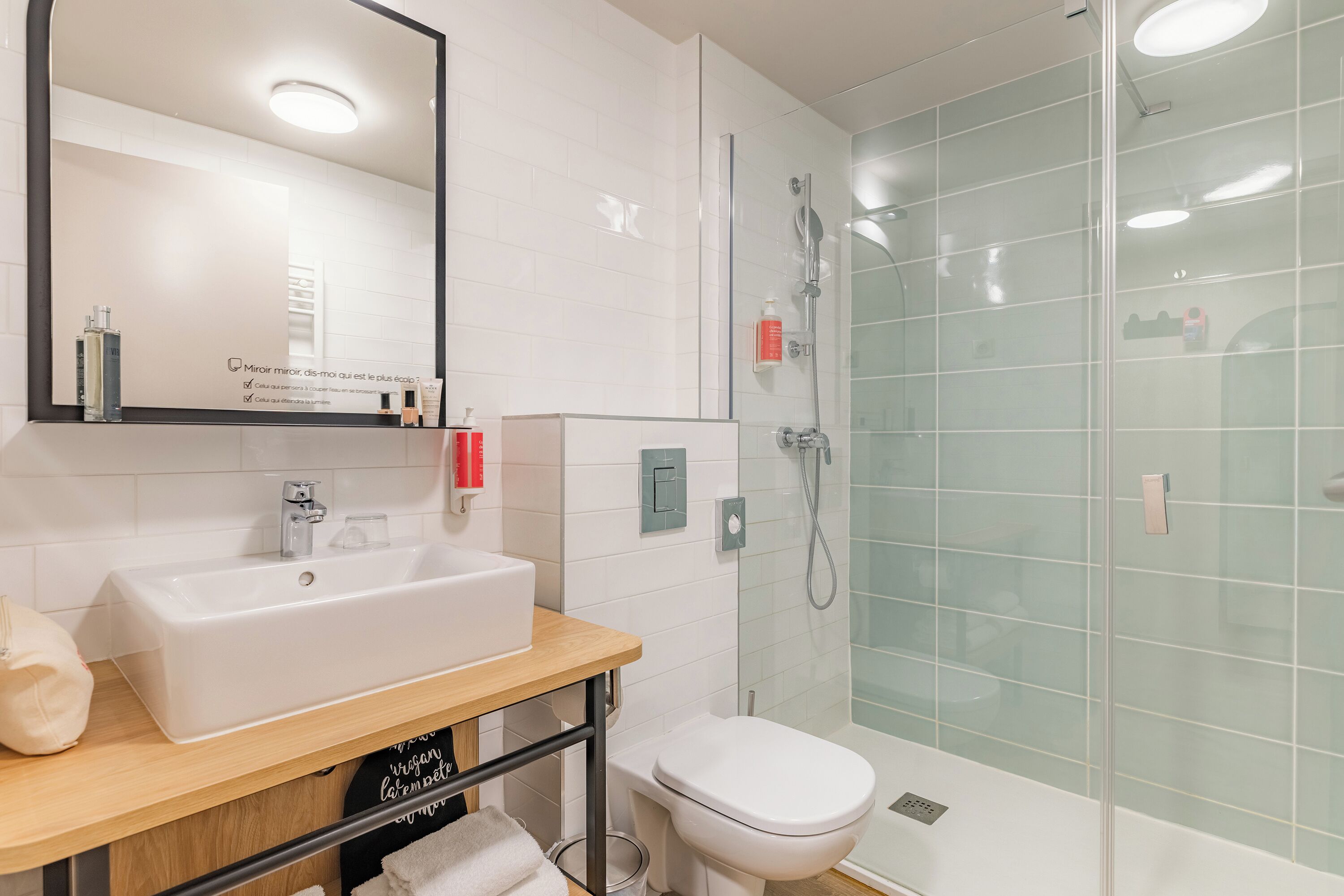 A modern bathroom with a white sink, mirror, and glass shower enclosure.