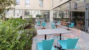 An outdoor seating area with tables and chairs, surrounded by greenery and a building with large windows. - Appart'City Confort Toulouse Diagora Labège (Labege)