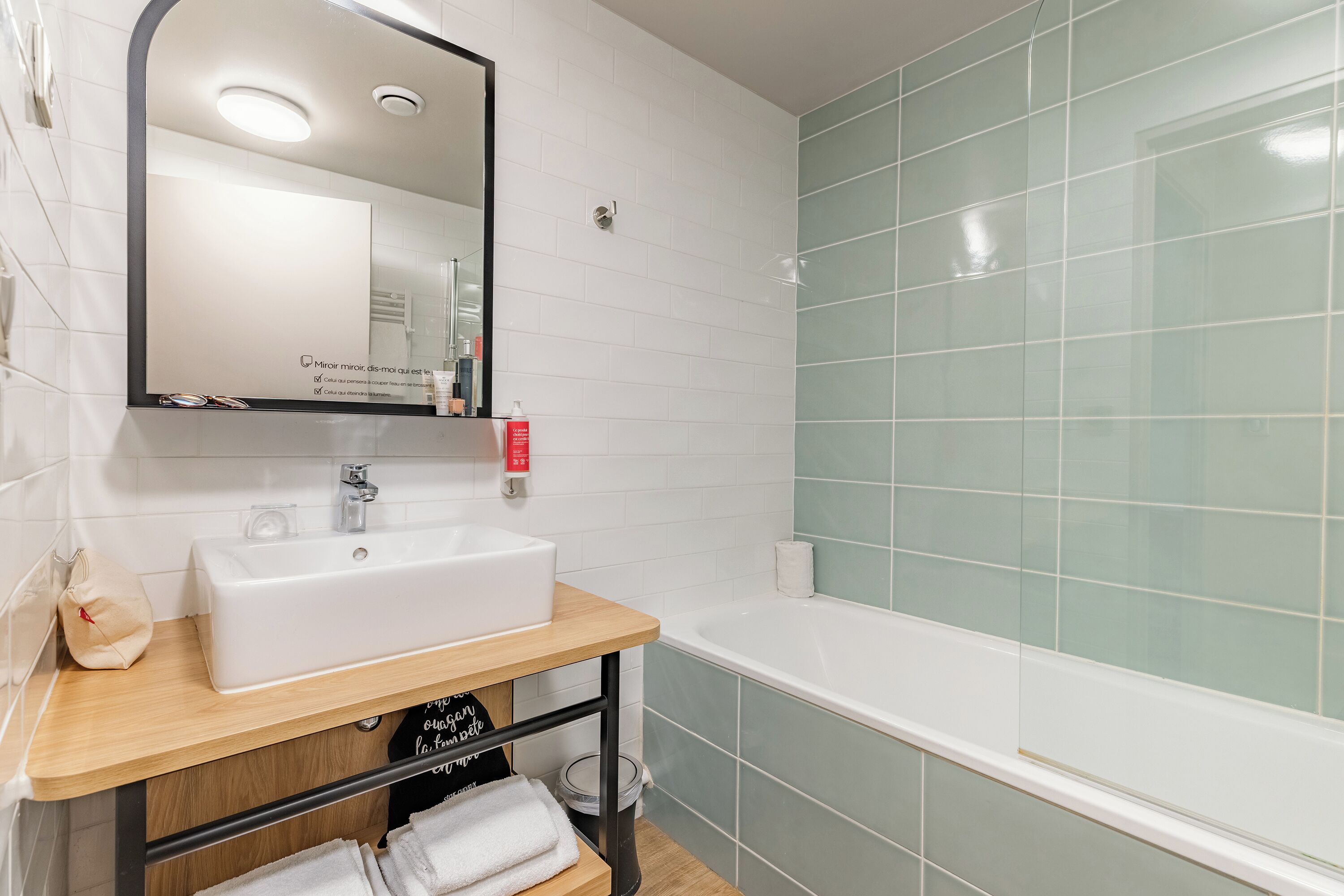 A bathroom with a white sink, mirror, and green-tiled shower area.