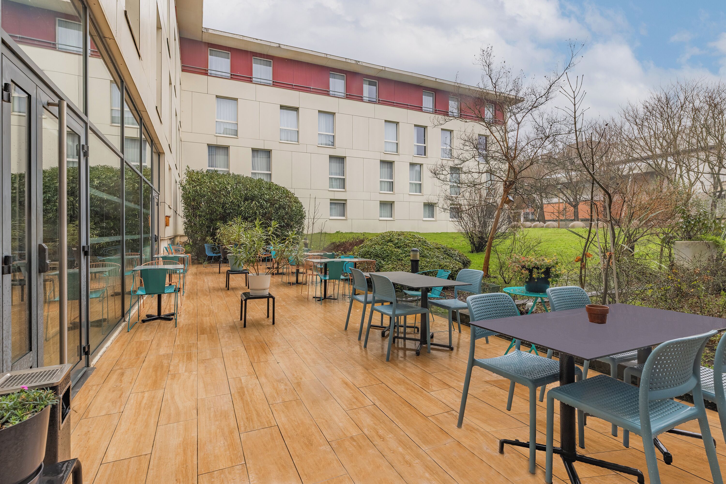 An outdoor patio with tables and chairs, a glass wall, and a building with multiple windows in the background.