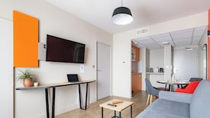 A modern living room with a sofa, a coffee table, a TV, and a small table with a laptop and a plant. - Appart'City Confort Toulouse Diagora Labège (Labege)