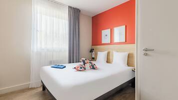 A hotel room with a bed, curtains, a headboard, and two framed pictures on the wall.