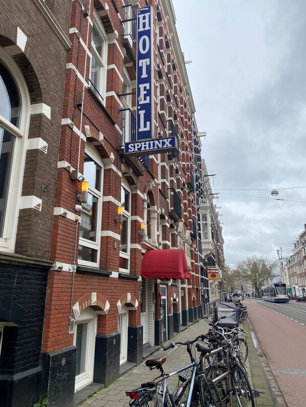 Un hôtel avec une enseigne bien visible portant l’inscription « HÔTEL SPHINX », sur un bâtiment en briques avec des éléments décoratifs blancs.