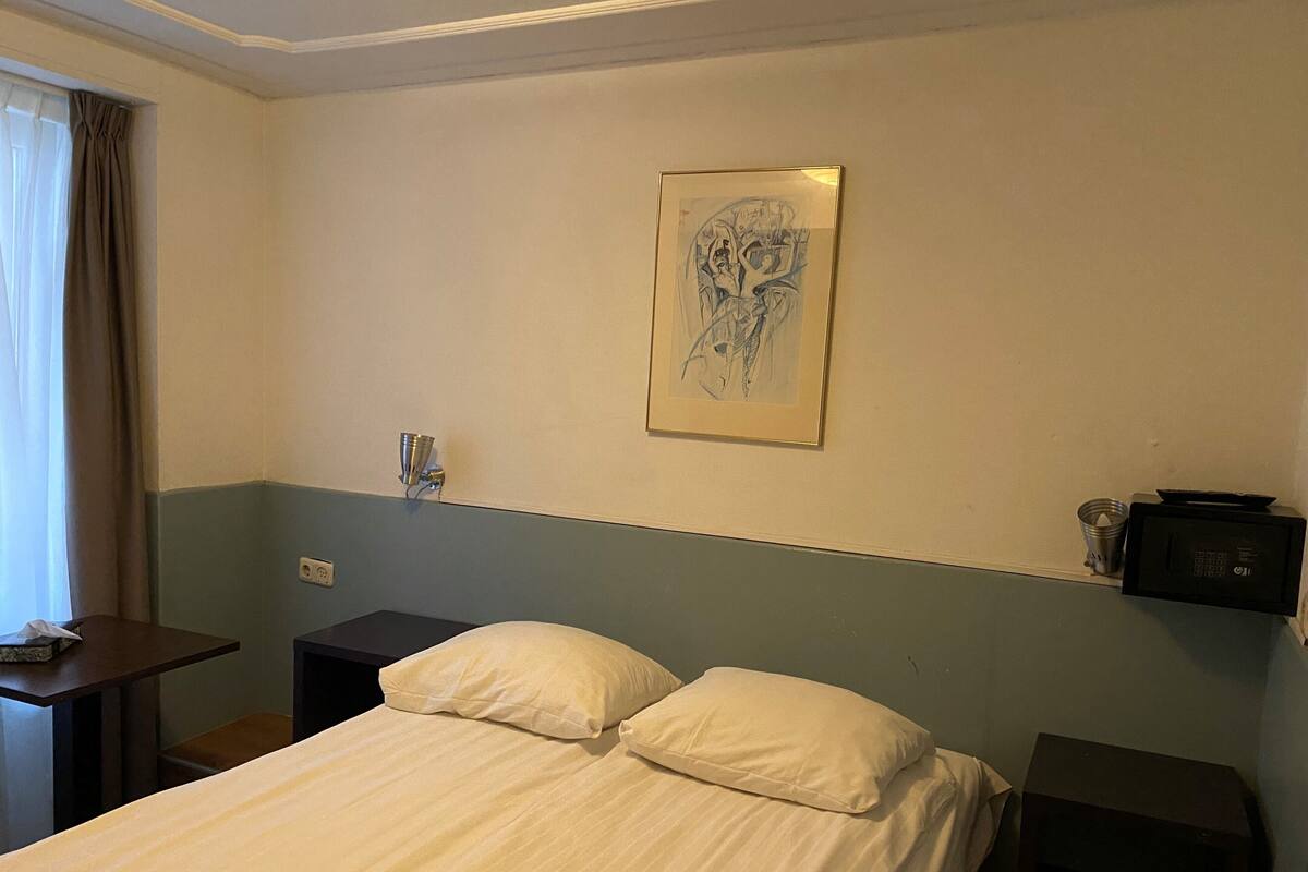 A hotel room with a bed, a nightstand, a lamp, a painting on the wall, and a microwave on the nightstand.