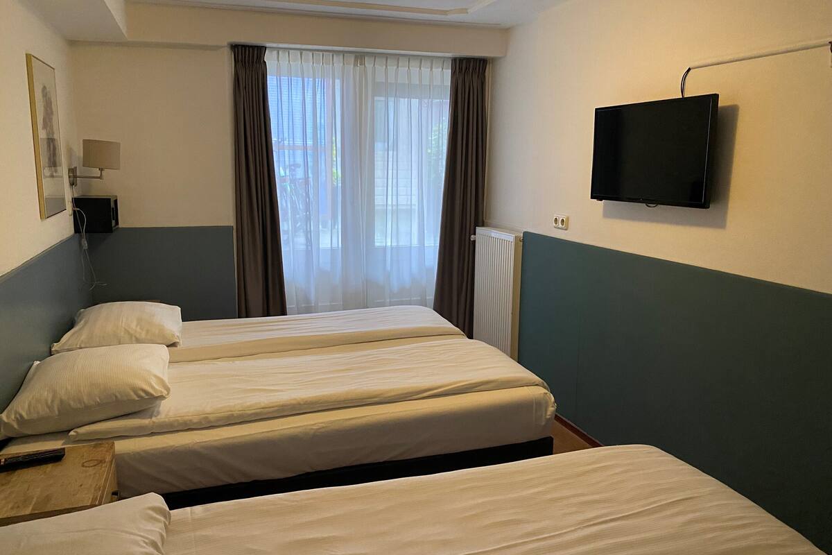 A hotel room with three single beds, a television on the wall, and a window with curtains.