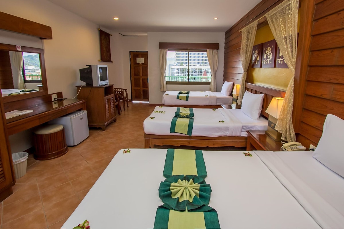 A hotel room with two beds, a desk with a television, a small refrigerator, and a window with curtains.