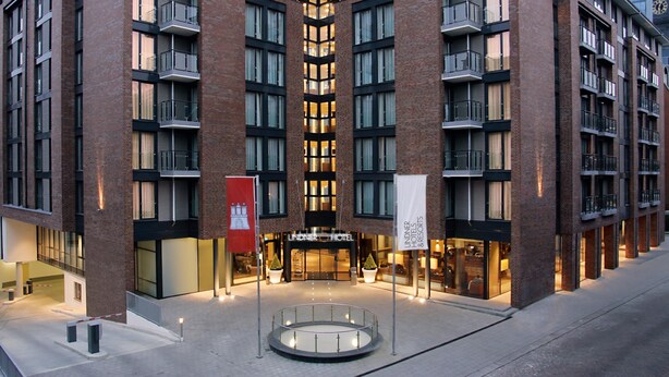 A modern hotel with a corner entrance, multiple balconies, and a prominent clock tower in the background. - Lindner Hotel Hamburg Am Michel, part of JdV by Hyatt (Hamburg)