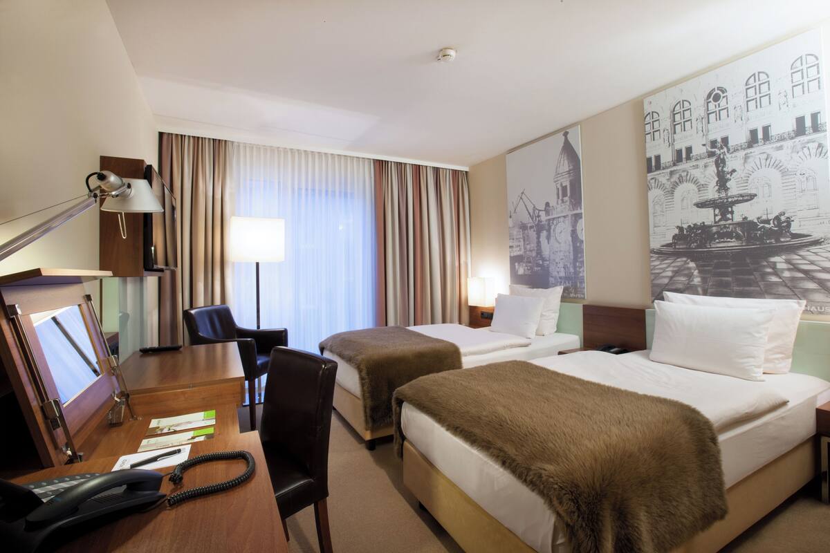 A hotel room with two beds, a desk with a telephone, a chair, and a lamp.