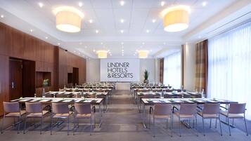 Une salle de conférence avec des tables et des chaises, une grande banderole sur laquelle on peut lire « Lindner Hotels & Resorts », et une plante dans un coin.