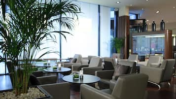 A modern lounge area with sofas and tables, large windows, and a potted plant.