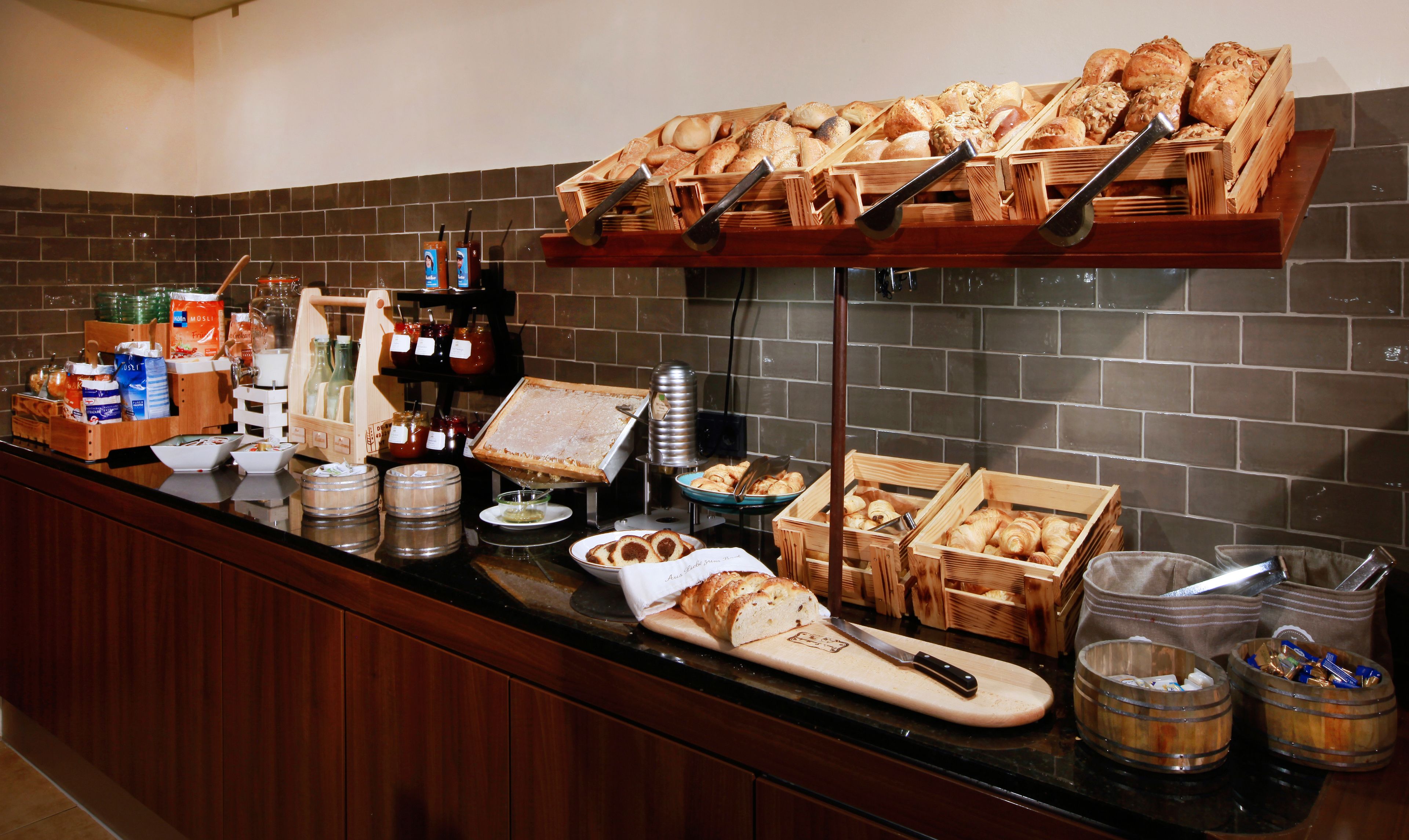 A buffet setup with various breads, pastries, and condiments.