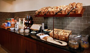 Una mesa de buffet con diferentes panes, bollería y salsas.