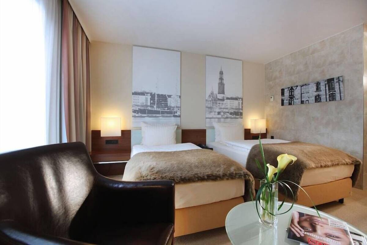 A hotel room with two beds, a sofa, a glass coffee table, and artwork on the walls.