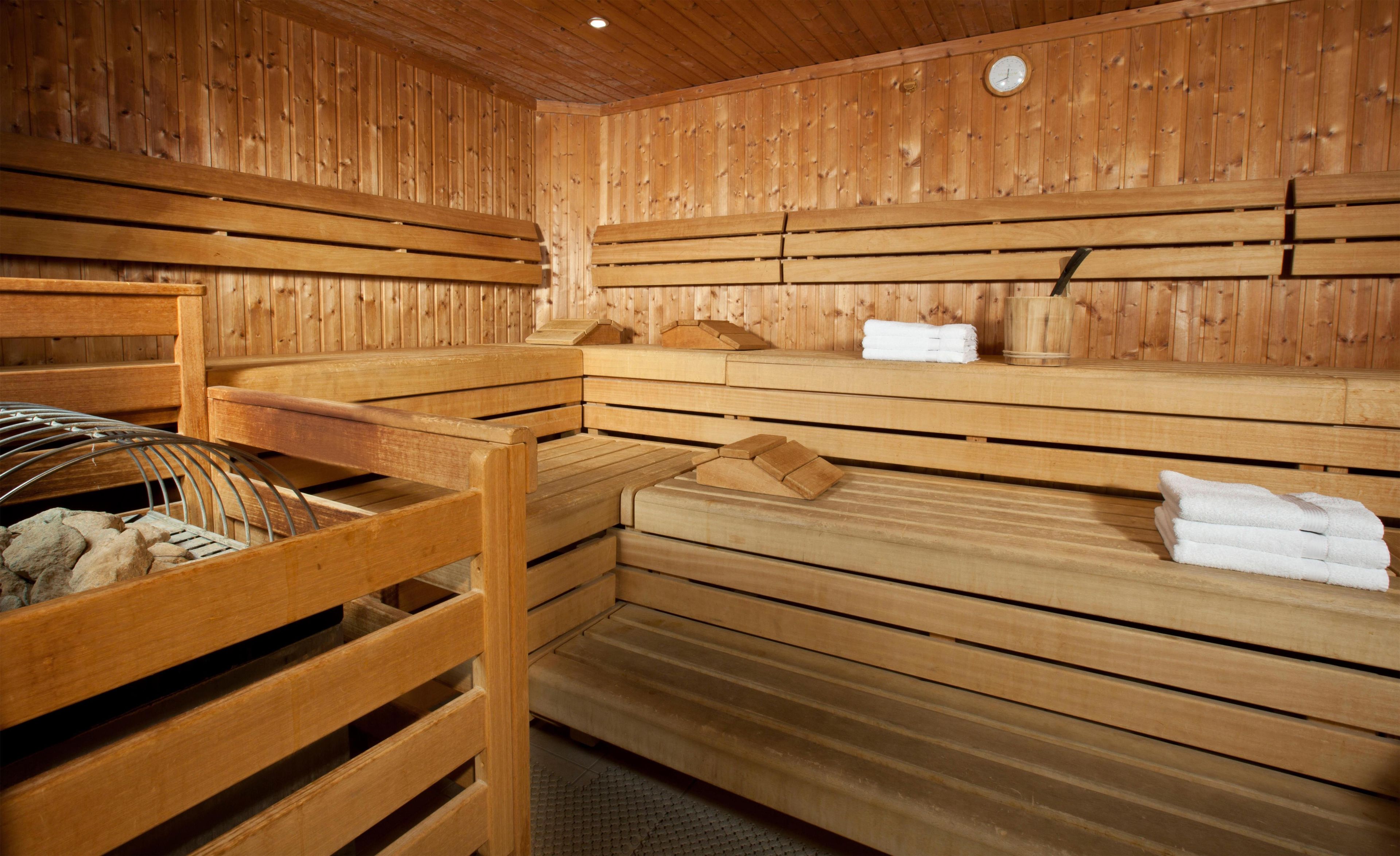 A sauna room with wooden benches and benches, towels, and a metal rack with stones.