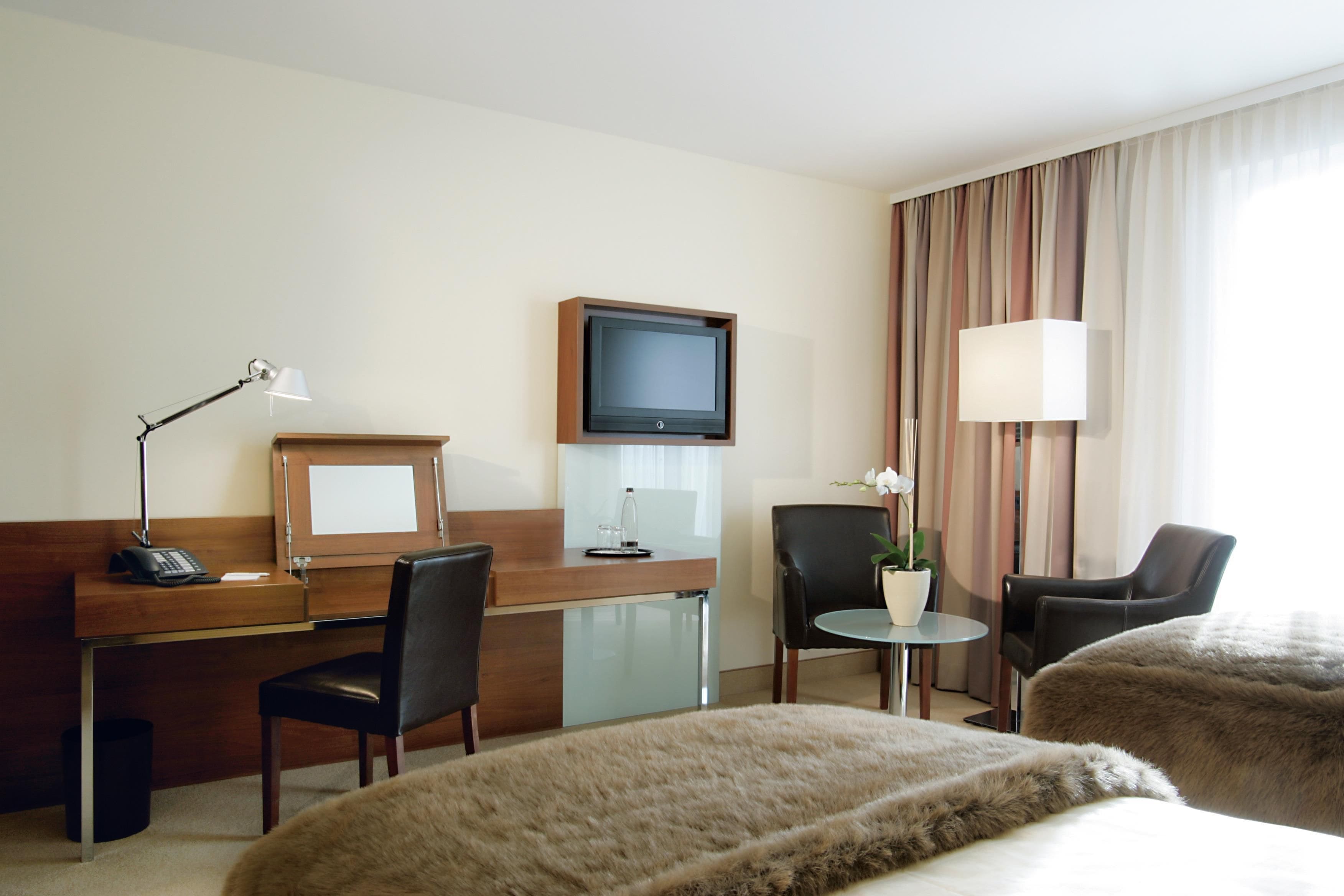 Habitació d'hotel amb escriptori, dues cadires, televisió, làmpada, taula petita amb una planta i dos llits.
