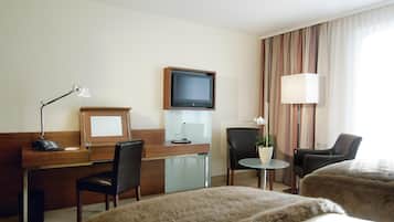 Habitació d'hotel amb escriptori, dues cadires, televisió, làmpada, taula petita amb una planta i dos llits.