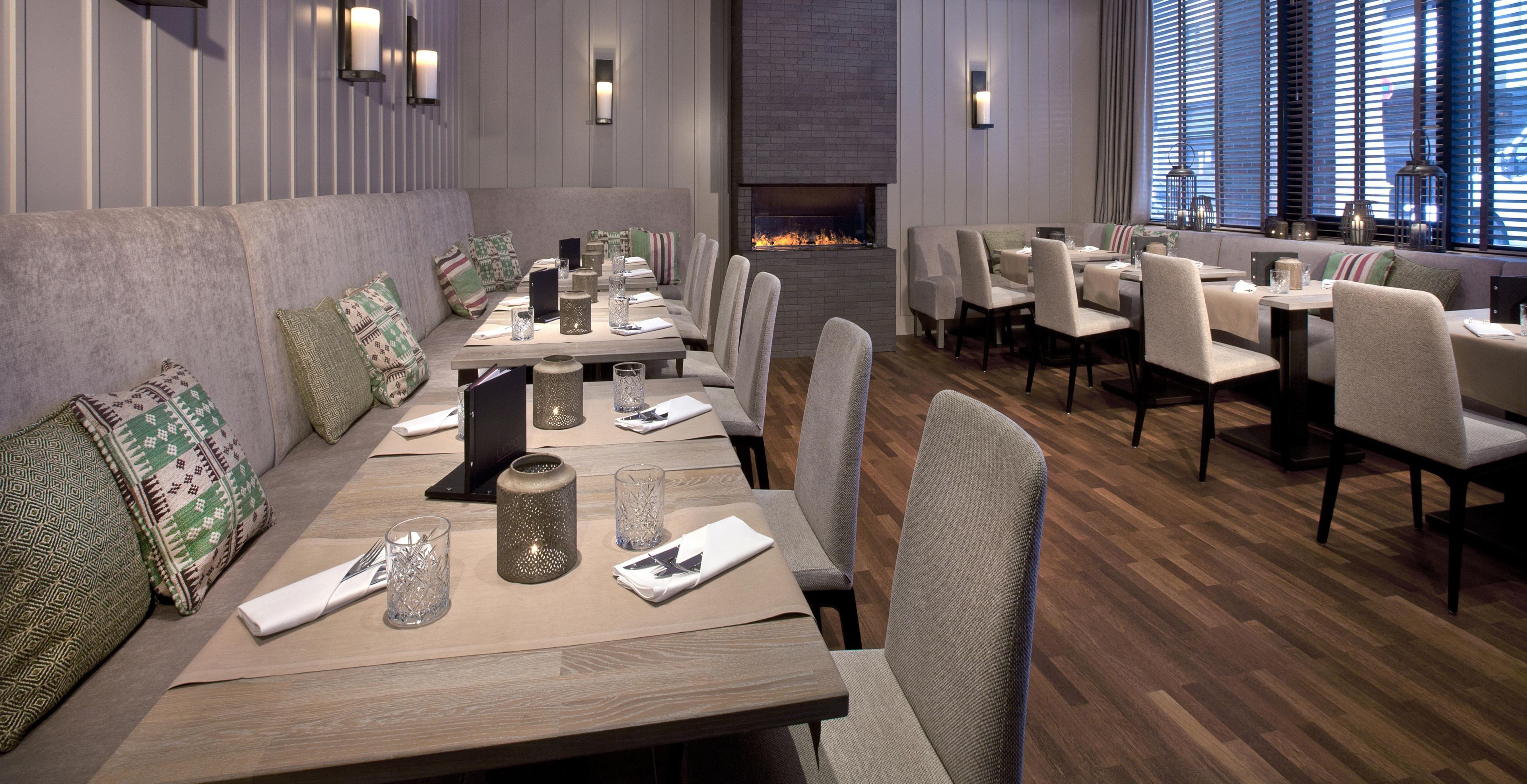 A restaurant with a long communal table, individual dining tables, cushioned seating, and a fireplace.