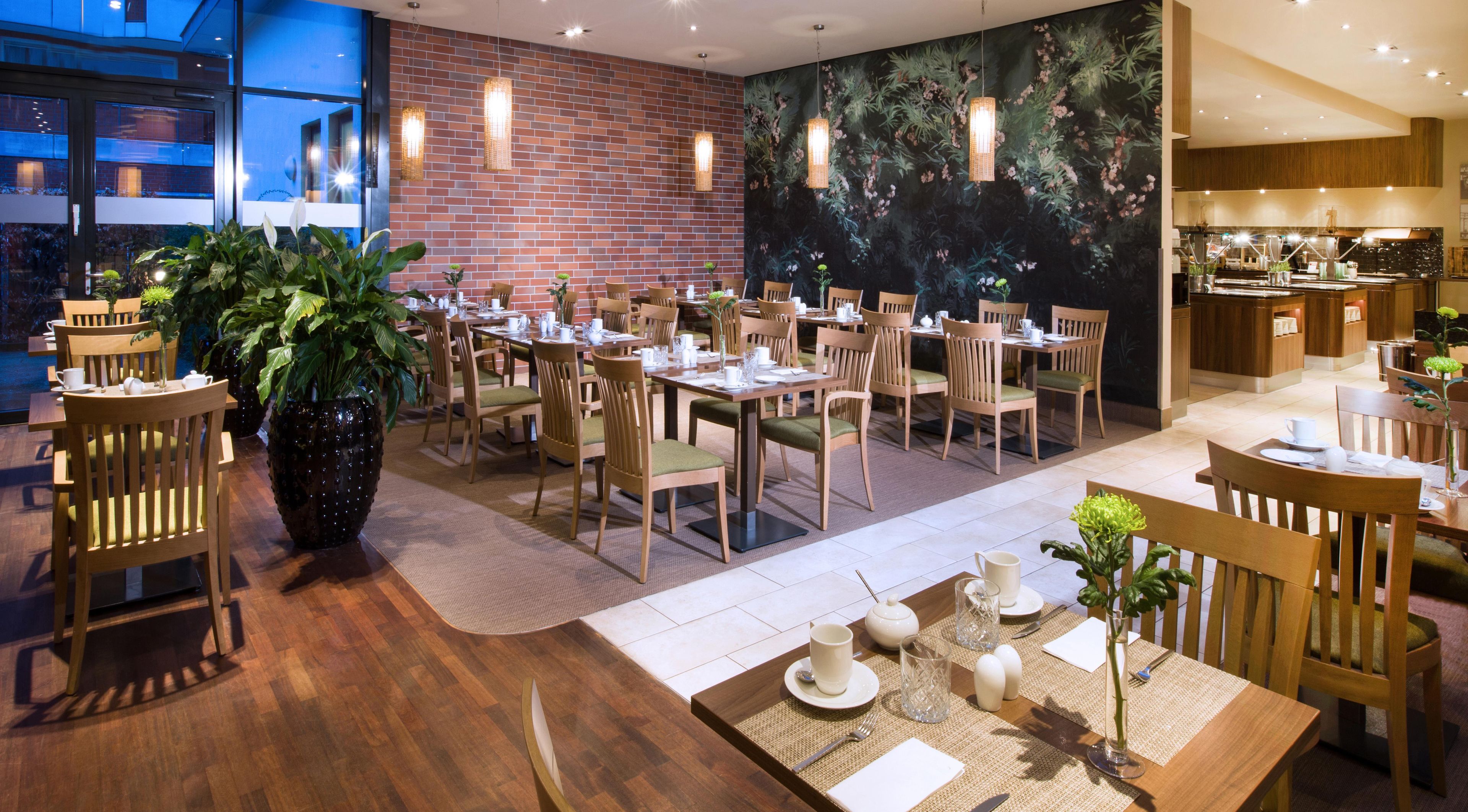 Un restaurante con varias mesas y sillas, una planta grande en maceta y una pared de ladrillo.