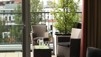 A balcony with wicker furniture, a potted plant, and a table with a pitcher and glasses.