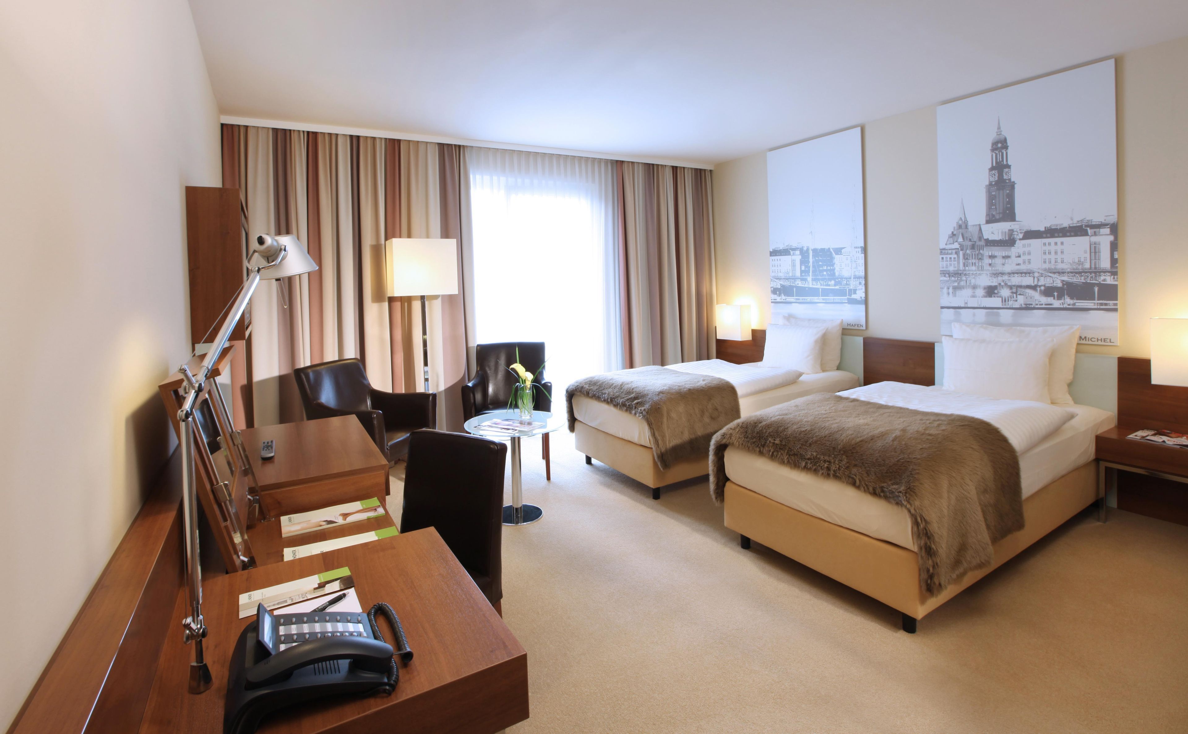 Une chambre d’hôtel avec deux lits, un bureau avec un téléphone, une chaise, une lampe et une vue sur le paysage urbain.