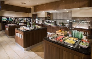 Zona de buffet con distintas estaciones de comida, con frutas, verduras y platos ya preparados.