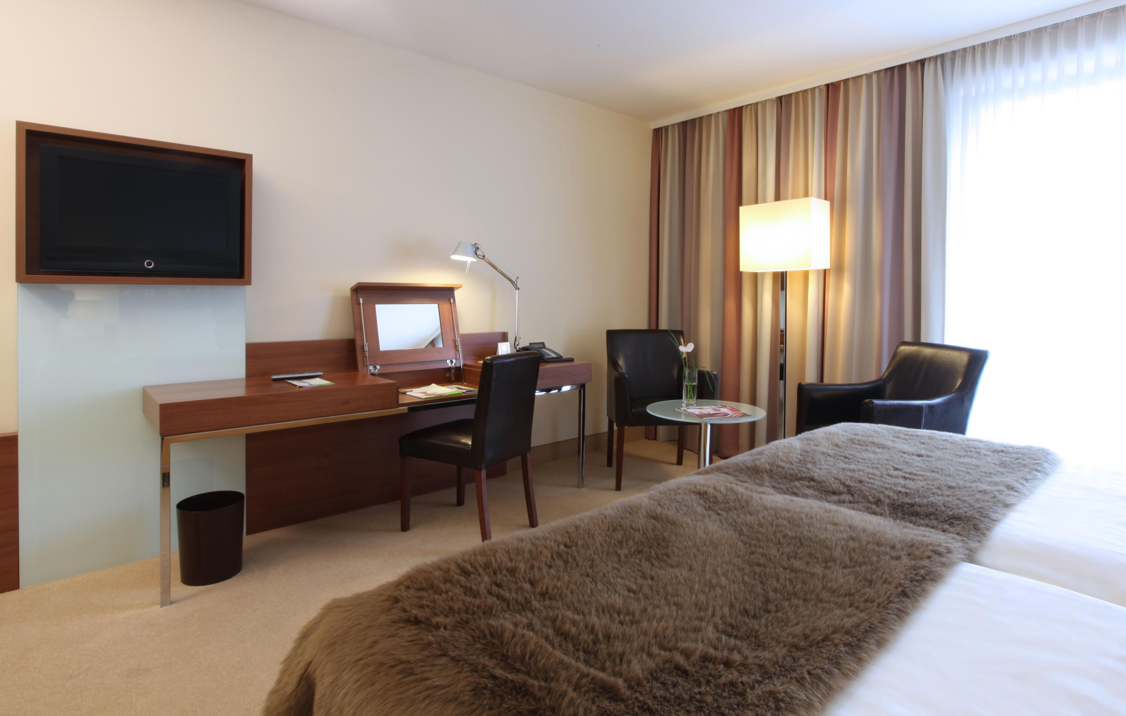 Habitació d'hotel amb llit, escriptori, cadires, televisió i làmpada.
