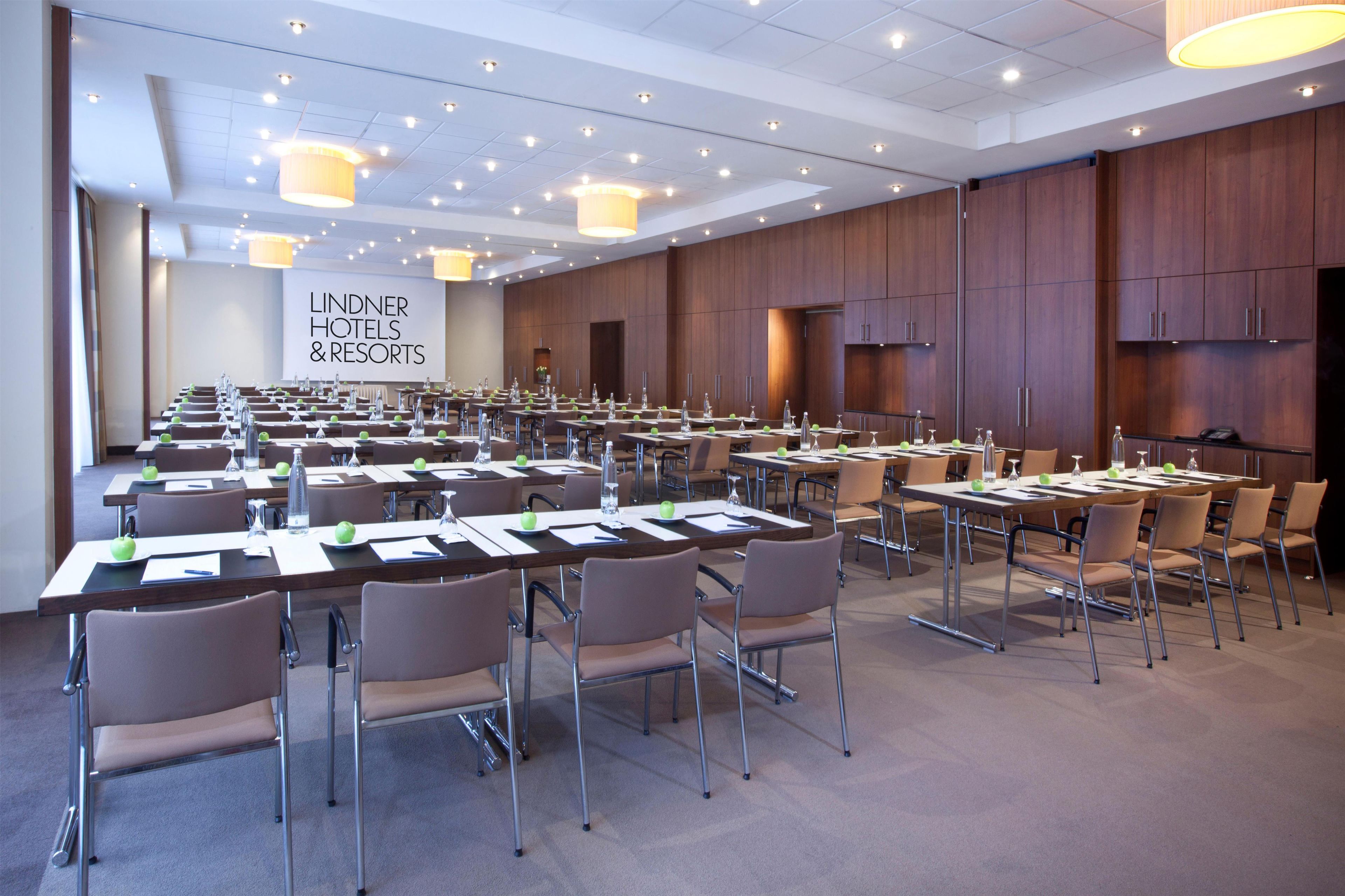 Sala de conferência com várias mesas e cadeiras, equipada com garrafas de água e blocos de anotações, em um ambiente de hotel.