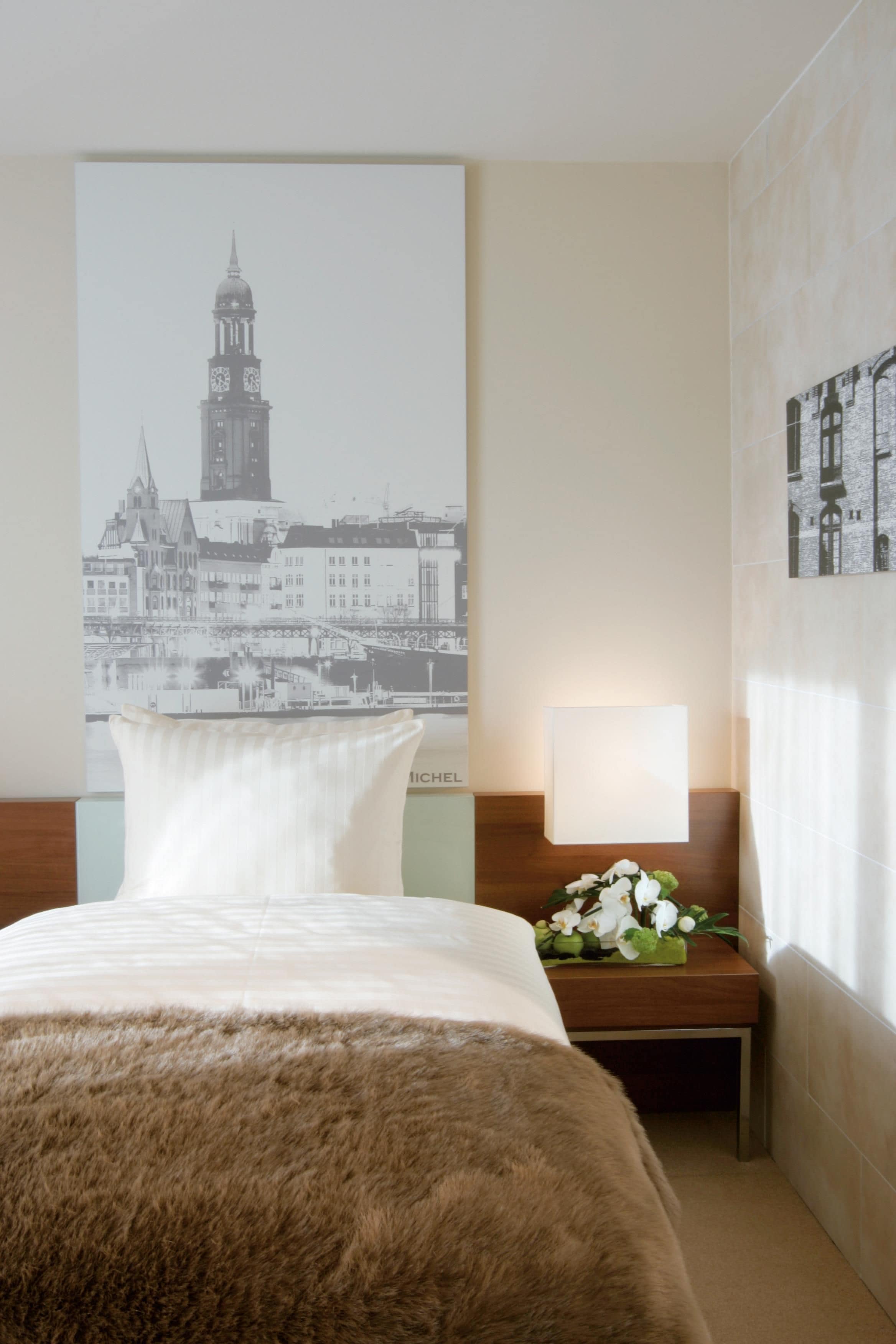Une chambre d’hôtel avec un grand lit, une table de chevet avec une lampe et une affiche représentant une vue de la ville accrochée au mur.