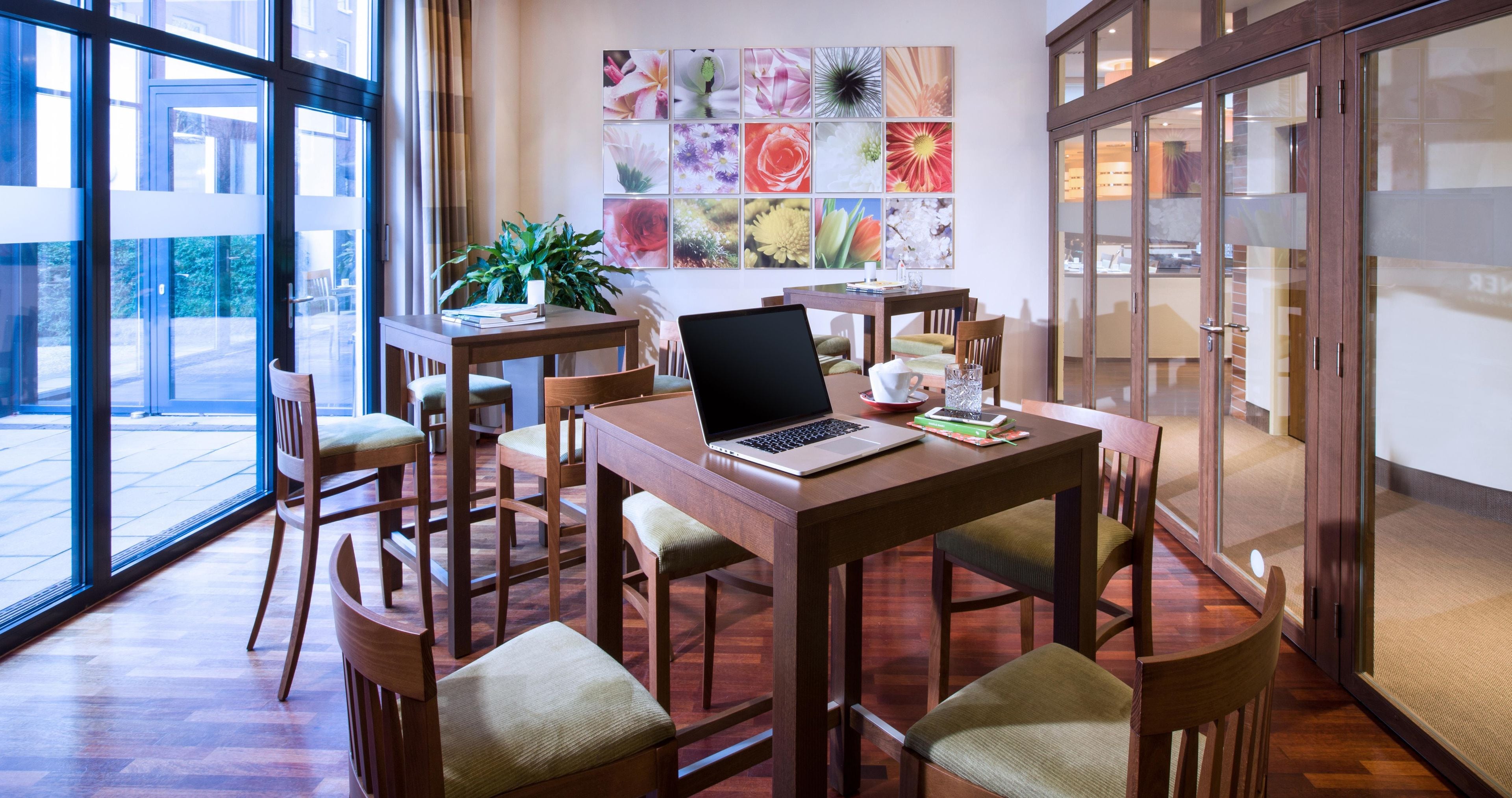 A modern dining area with a laptop on a table, surrounded by chairs, and a wall with a floral art display.
