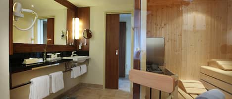 Un baño moderno con un espejo grande, un lavamanos, un inodoro y una zona de sauna de madera.